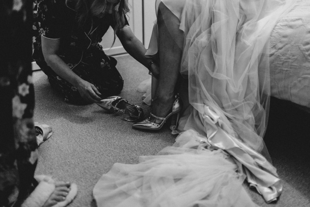 bridesmaid helps to put bride's shoes on at before her wedding