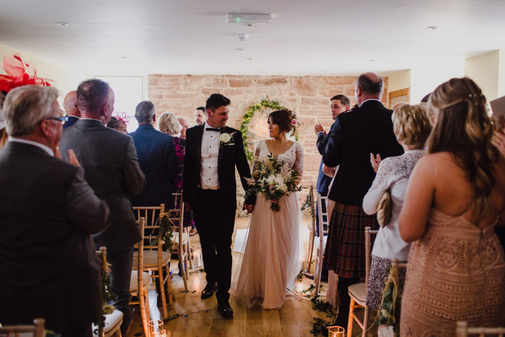 bride and groom walk up the aisle in the ceremony room at Boswell's Coach House after their Ayrshire wedding
