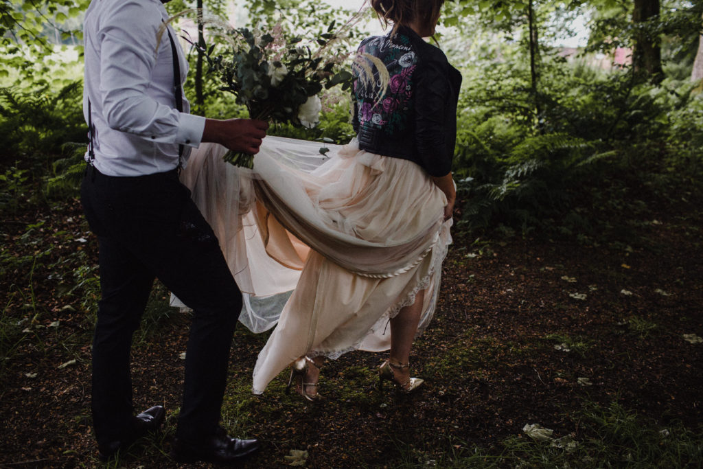 groom helping with bride's dress as they walk through the woods at Boswell's Coach House Ayrshire