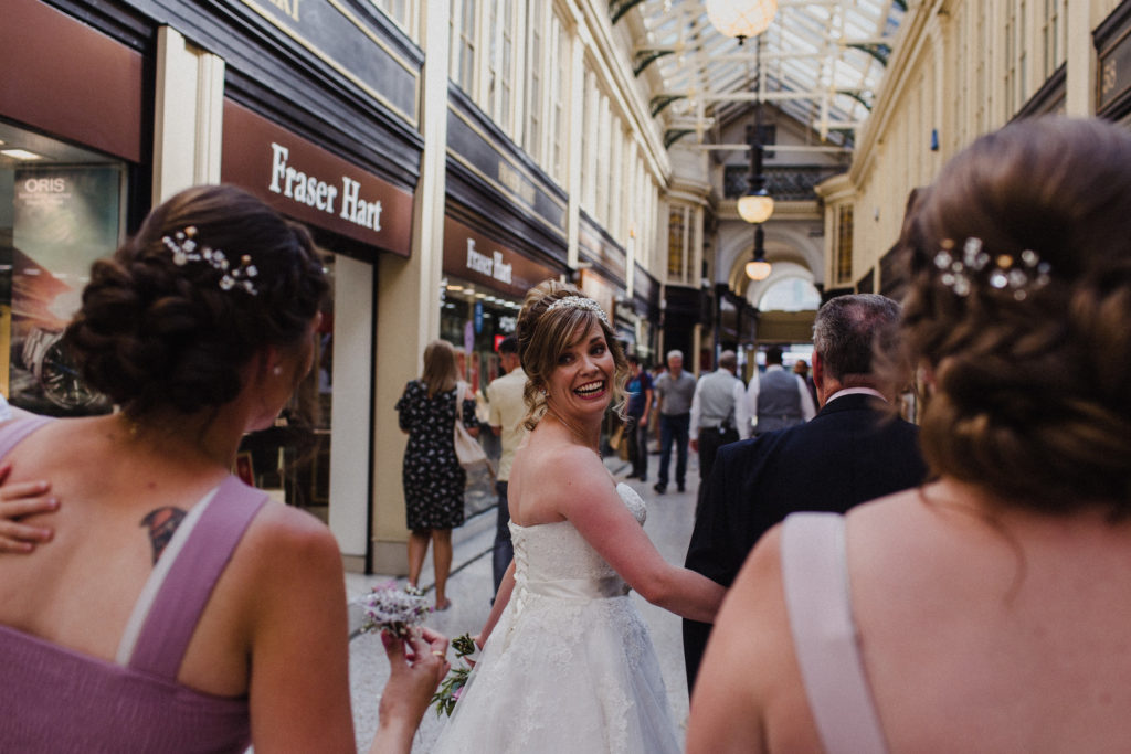smiling bride walking through the Argyle Arcade with her father towards her wedding ceremony at Sloan's Glasgow