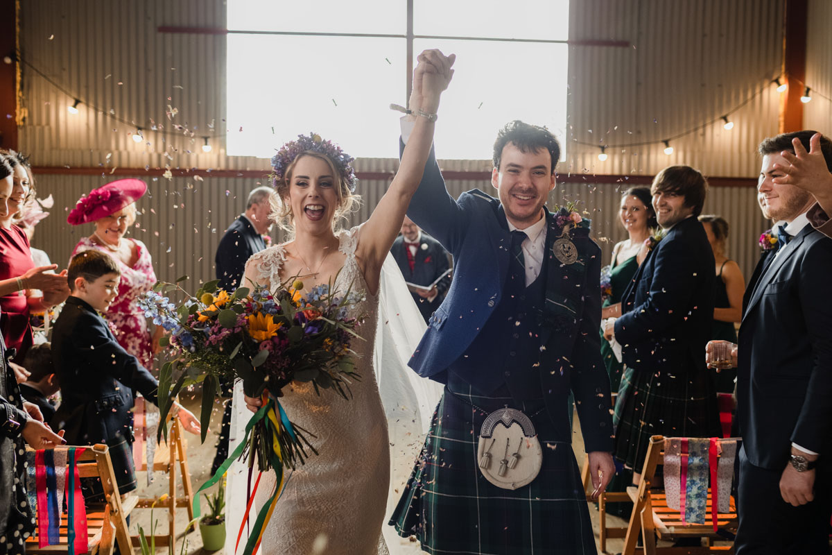 Bride and goom laugh as walking through confetti after their ceremony at Dalduff Farm