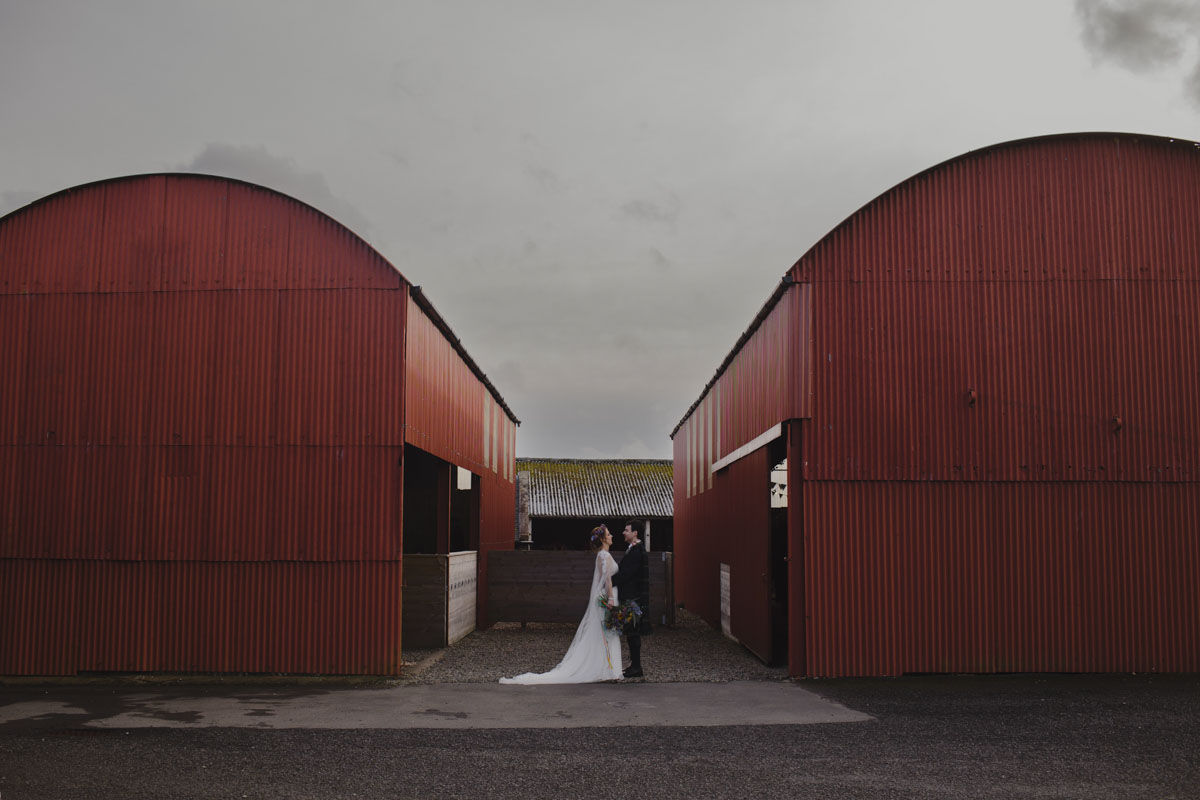 Wide picture of bride and groom in front of red barns