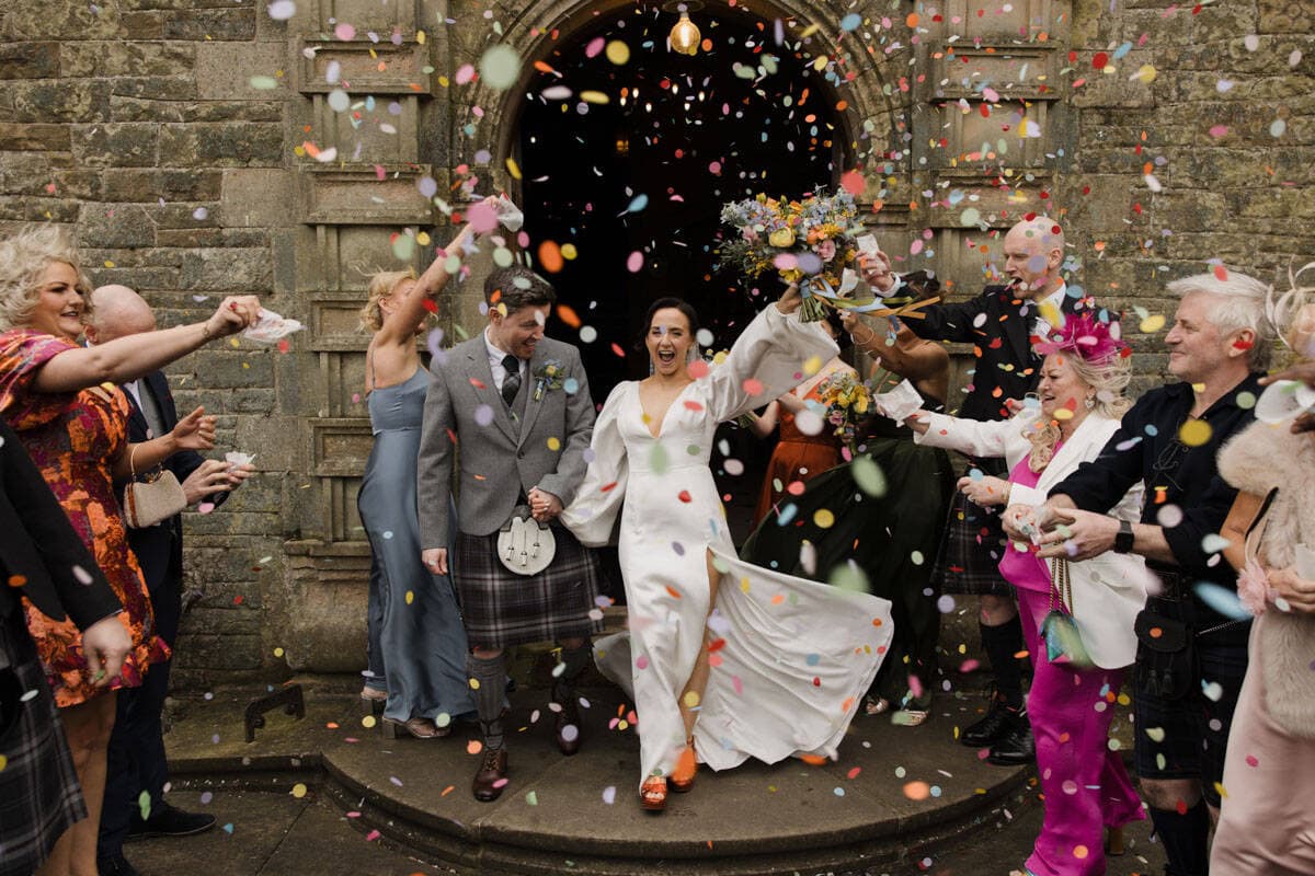 Joyful wedding celebration at Rowallan Castle with confetti and stormy skies.