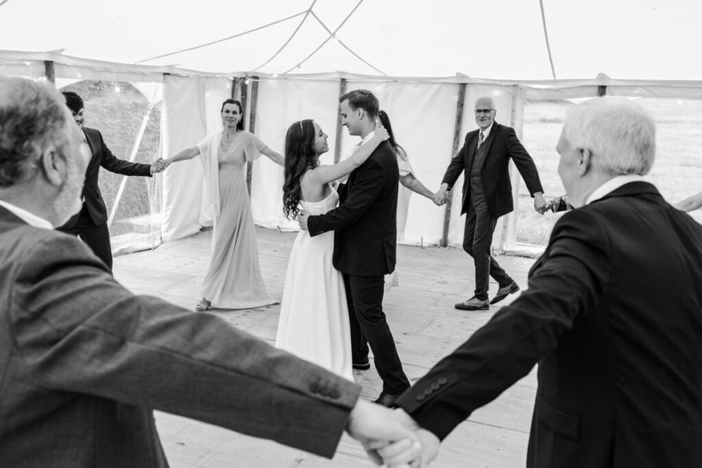 Wedding guests dancing and holding hands at Scottish venue, black and white photo.