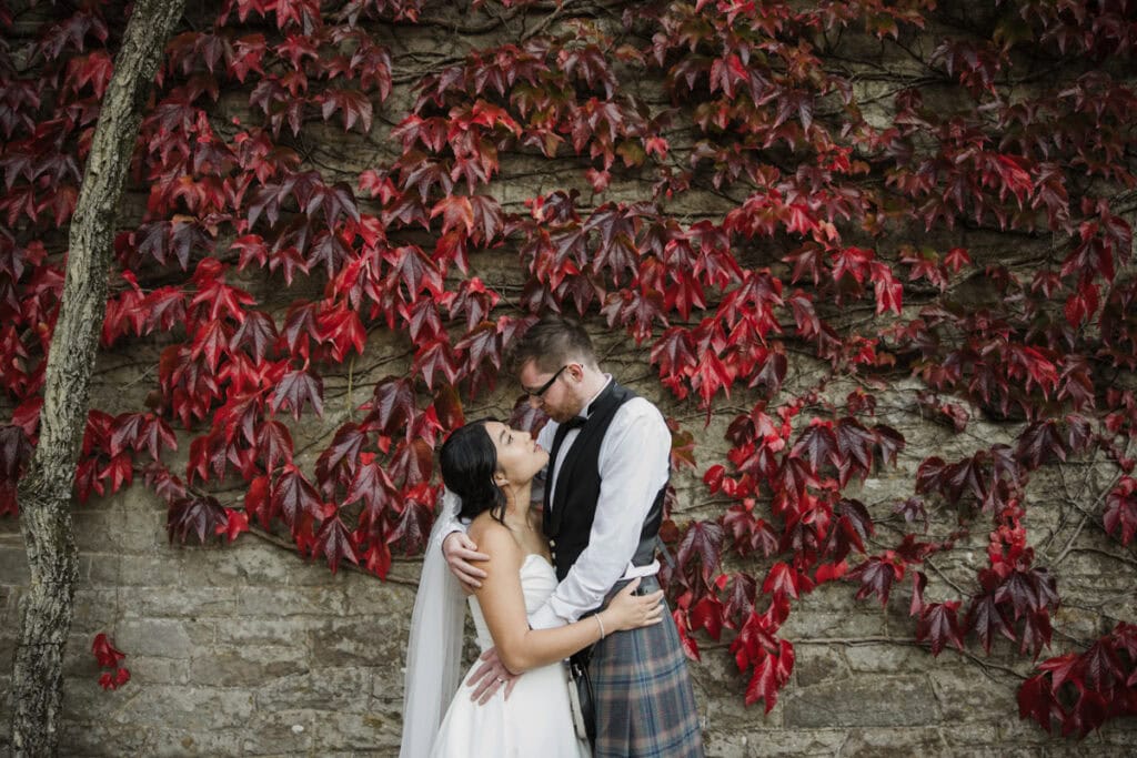 Romantic wedding couple embracing against vibrant red autumn leaves at Rowallan Castle, Ayrshire.