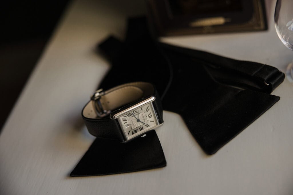 Elegant wristwatch on a white surface with black accessories, ready for a wedding day.