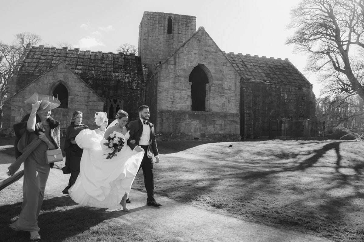 Wedding couple walking outside Dunglass Estate with guests, black and white photo.
