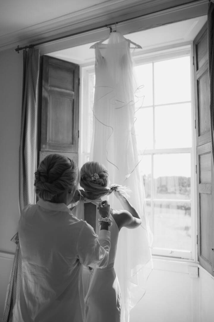 Bride preparing dress in bright room with open window, Scottish venue setting.