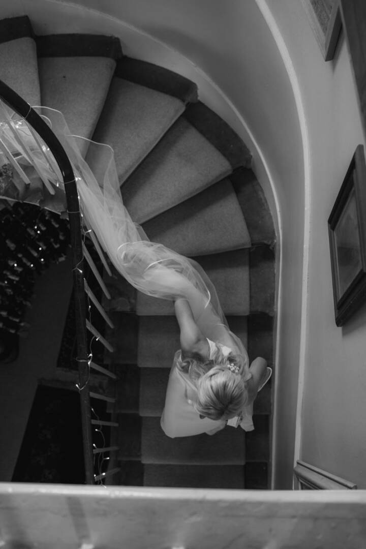 Bride descending spiral staircase in black and white wedding photo.