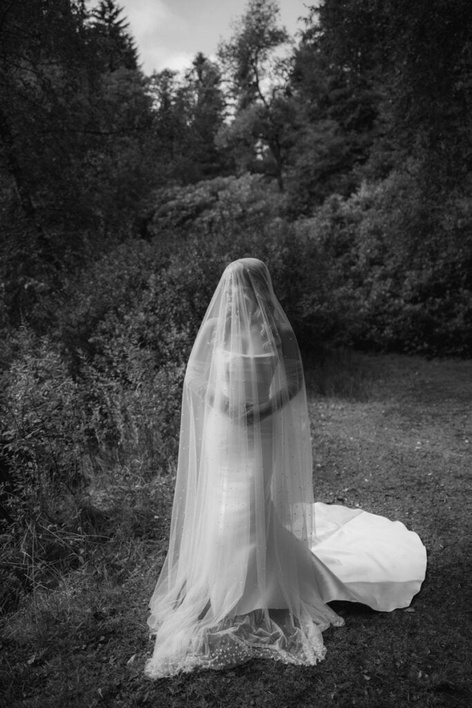 Bride in veil standing in Scottish woodland for wedding photography.